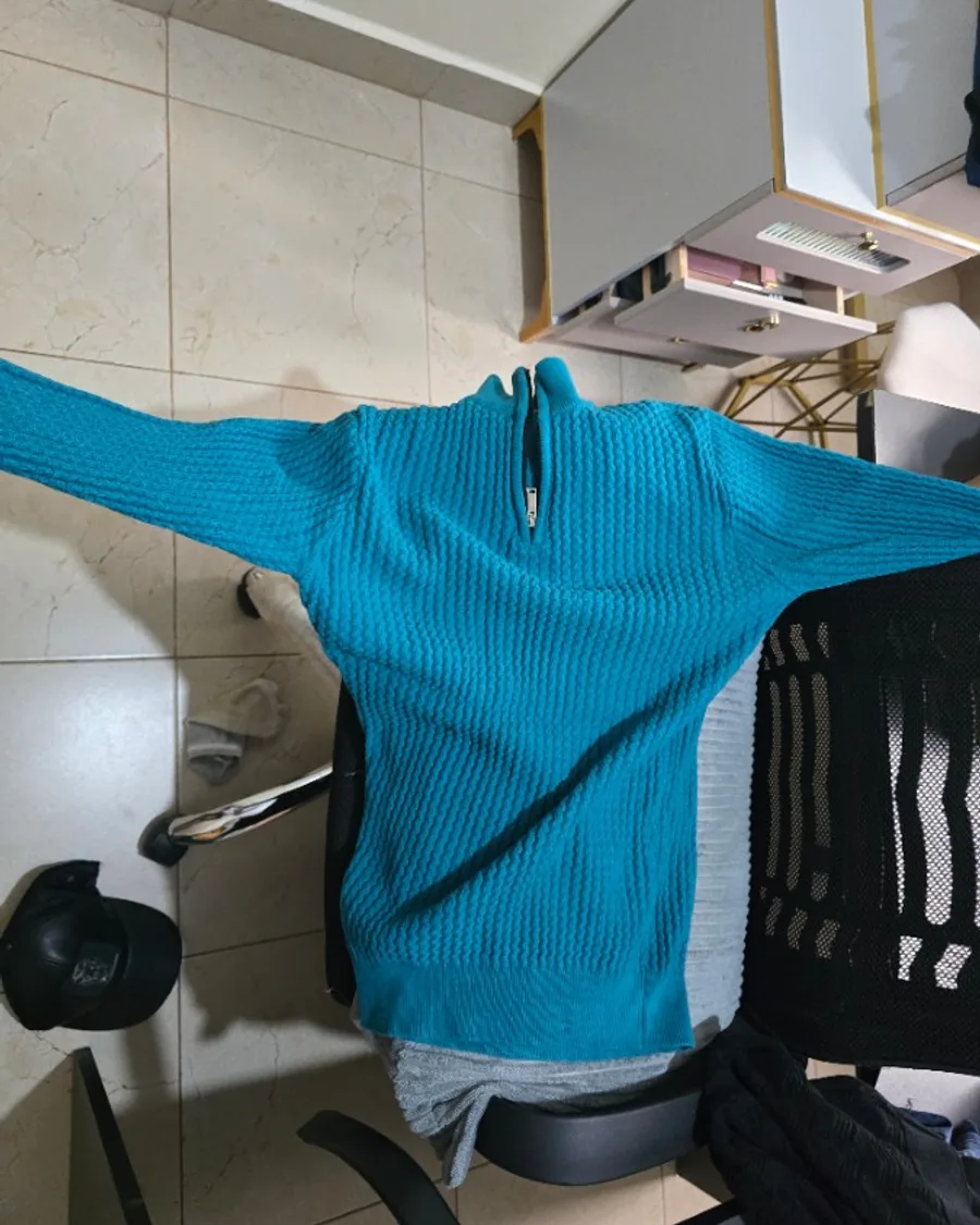 A teal half-zip knit draped over an office chair