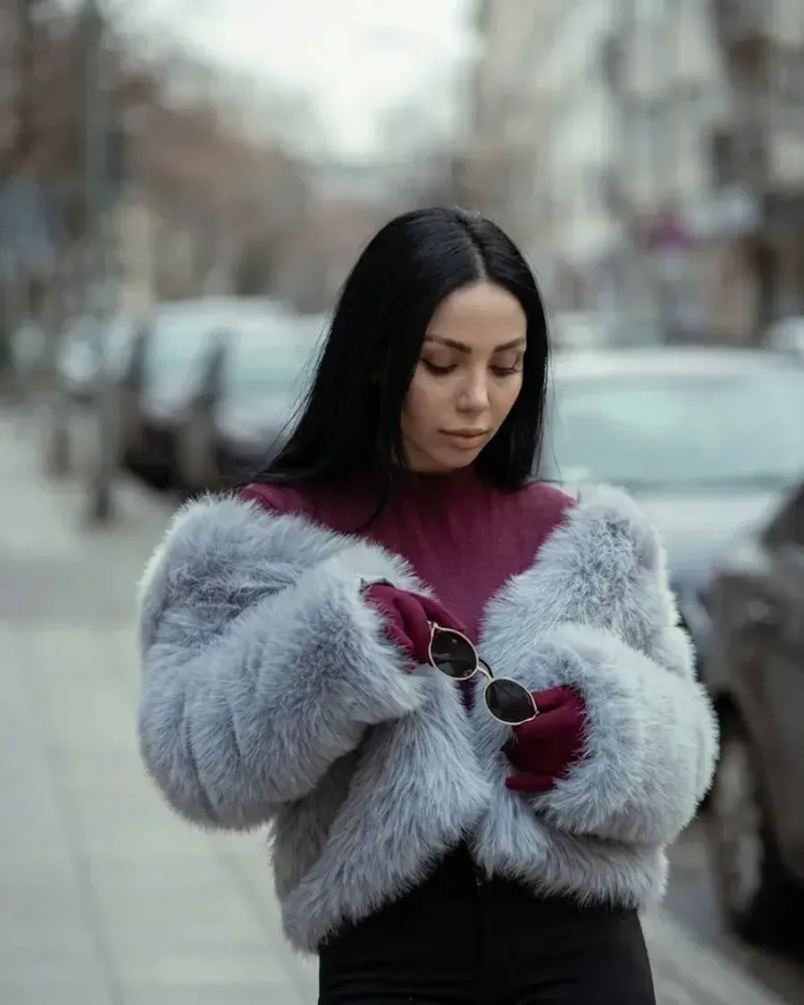 A woman in a grey faux fur jacket over a burgundy turtleneck on an overcast street