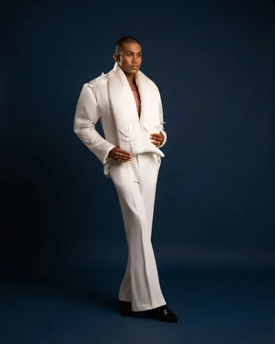 A model in a white draped suit with wide trousers against a navy studio backdrop
