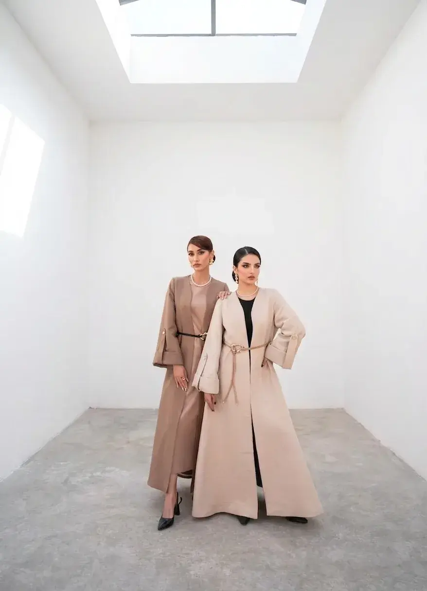 Two women in camel and cream coats, styled by Clad9